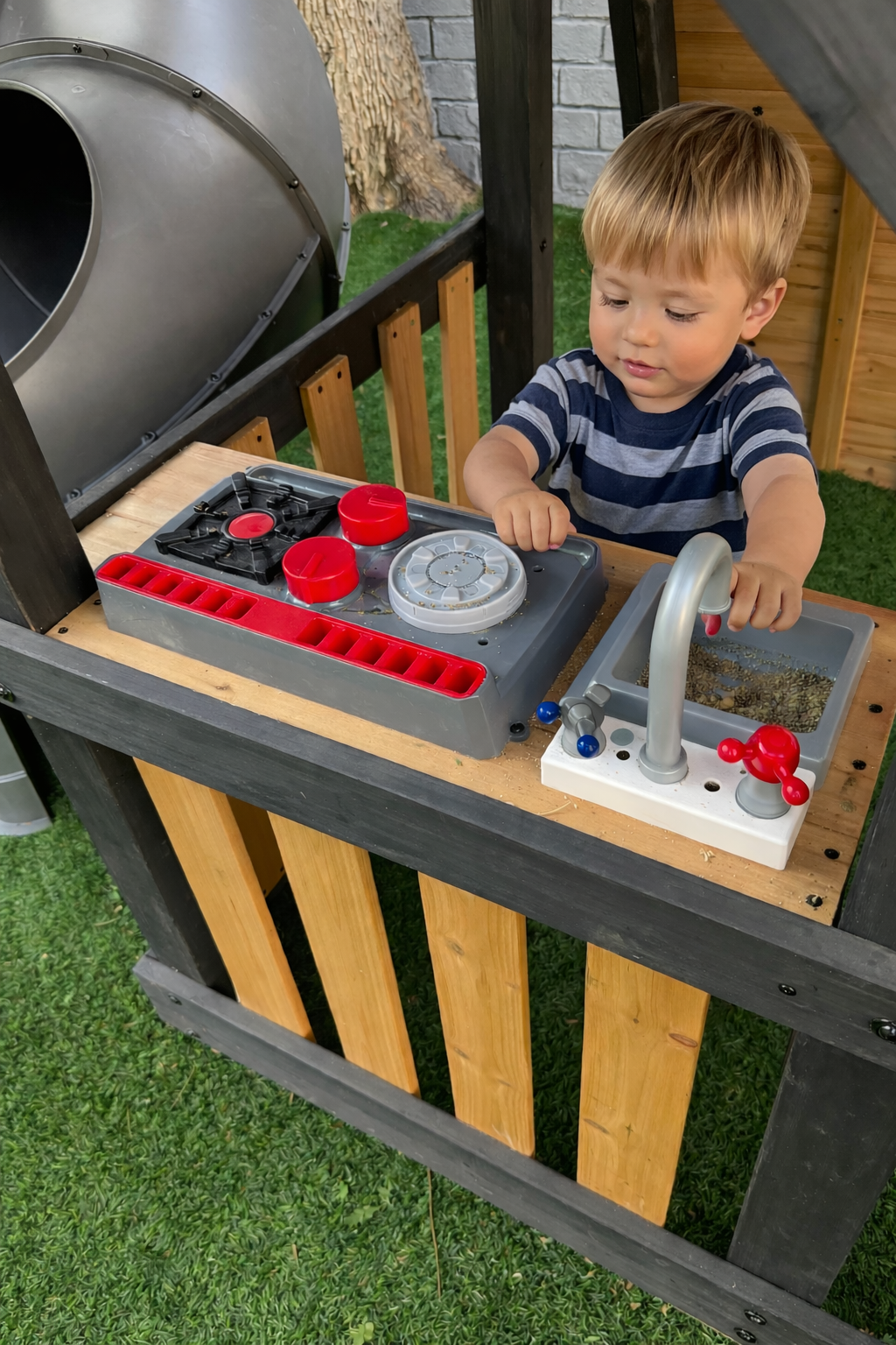 Niño jugando en cocinita de madera dentro del área de juegos de Diversitopia, junto a resbaladilla tubular.