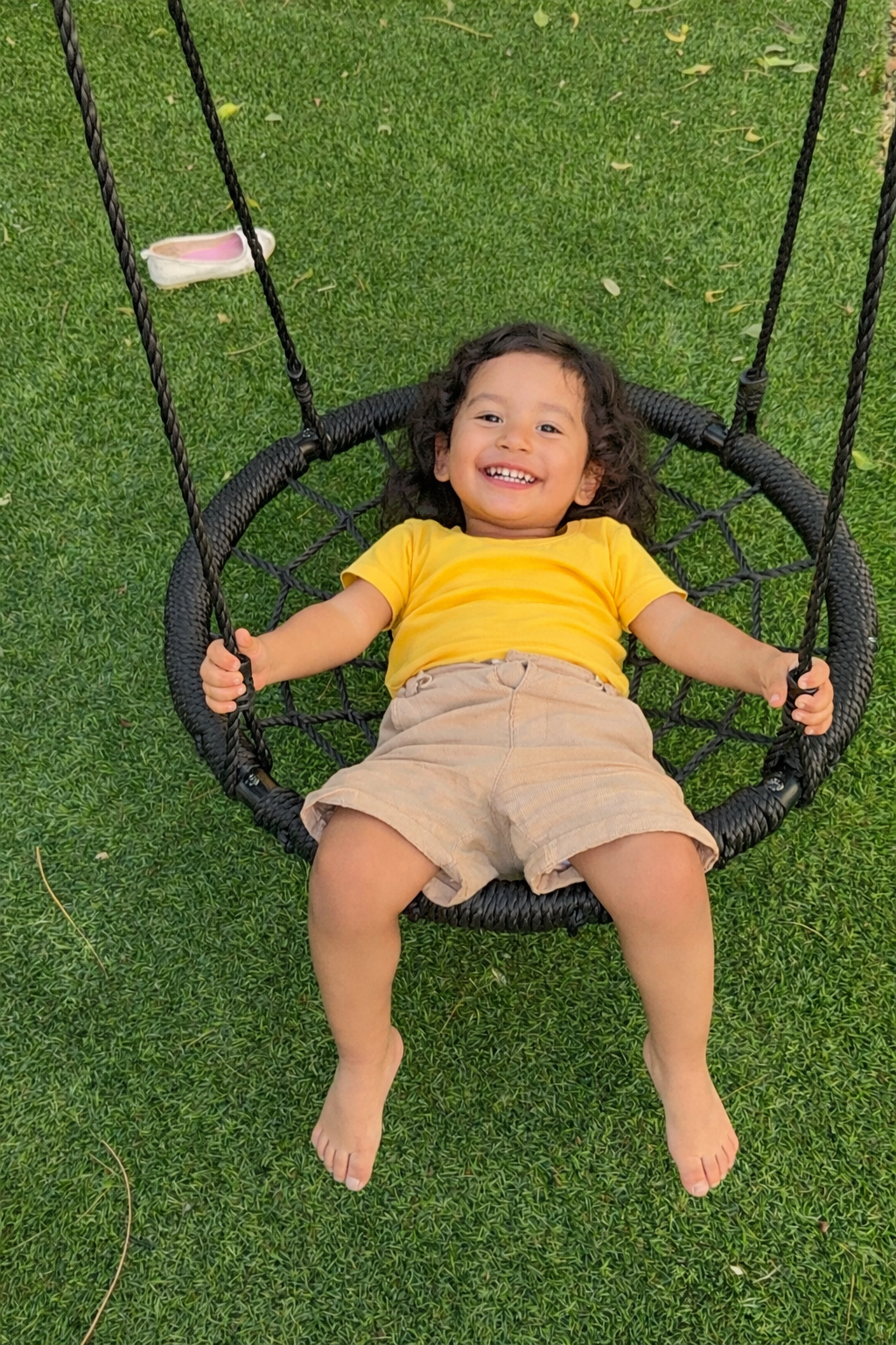 Niño sonriendo en columpio tipo nido sobre pasto sintético en la zona de juegos de Diversitopia.