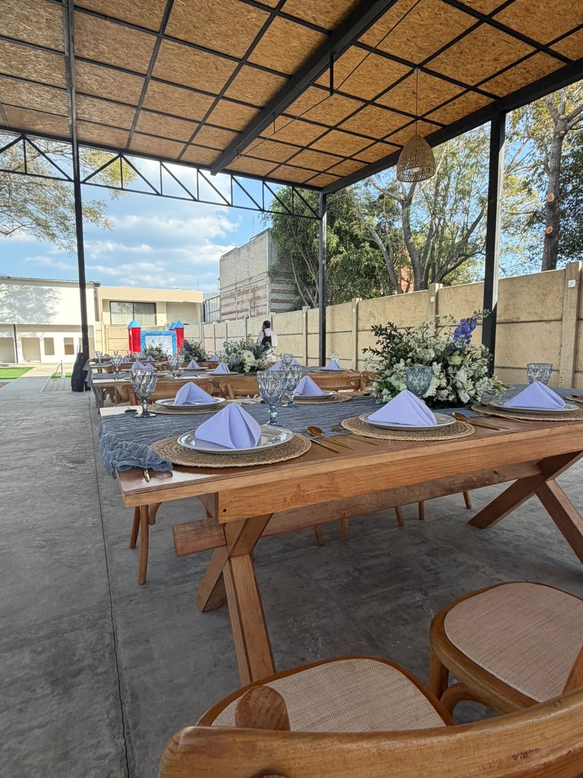 Montaje de mesa larga con cristalería y flores en terraza techada; espacio para celebraciones en Diversitopia.